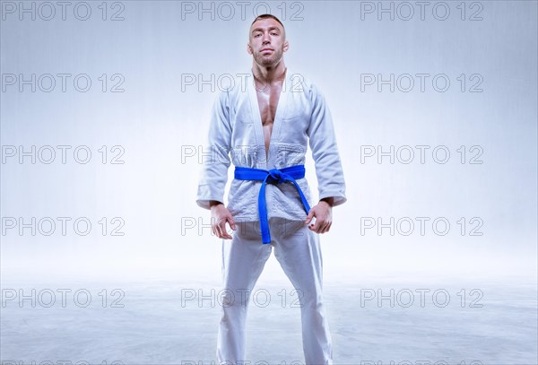 Athlete in a kimono with a blue belt stands on a light background. The concept of karate and judo.