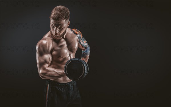 Young muscular guy pumping biceps with dumbbells. Concentrated flexion. Fitness and nutrition concept.