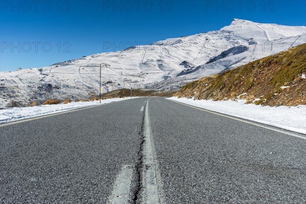 Empty road leading towards snow-covered mountain under a clear blue sky