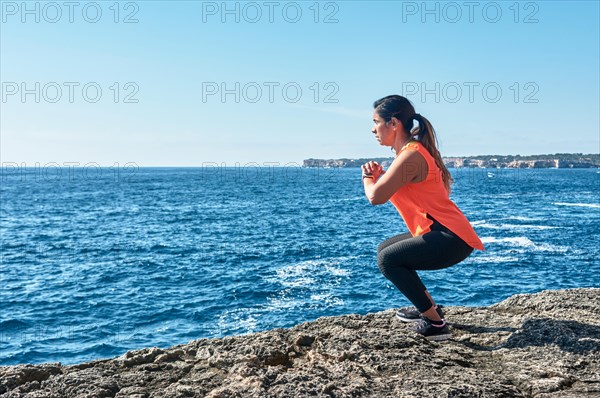 A woman crouches by the ocean on a sunny day