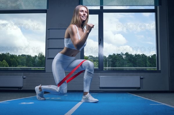 Charming girl does an exercise called lunges. Elastic band for training. The concept of fitness