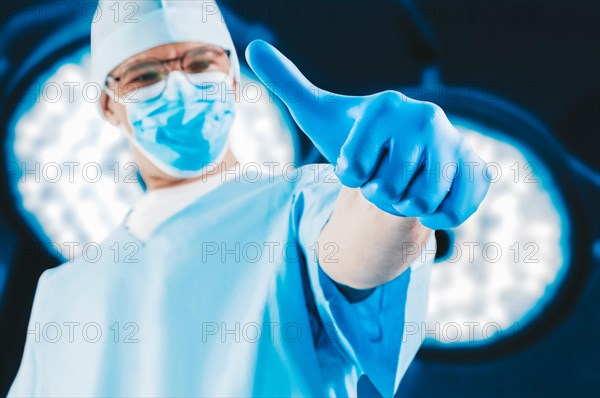 The doctor against the background of surgical lamps shows a raised finger. Medicine concept.