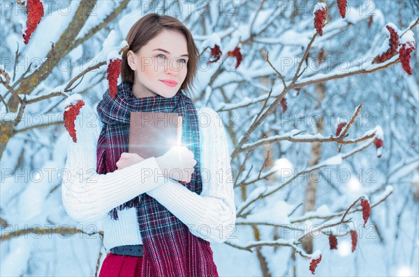 Portrait of a charming girl who hugs a book in the winter forest. Concept of Christmas