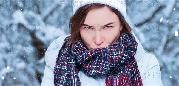 Portrait of a charming woman with a displeased expression on the background of snowy trees. Christmas holidays concept.