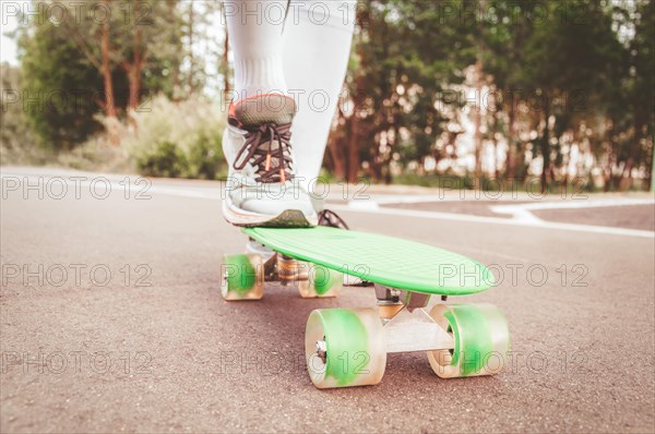 Images of a leg standing on a skateboard. Sunny evening in the park. Skateboarding concept.