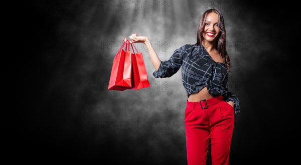 Beautiful happy brunette with red packages in her hands. Black background. Concept for discounts