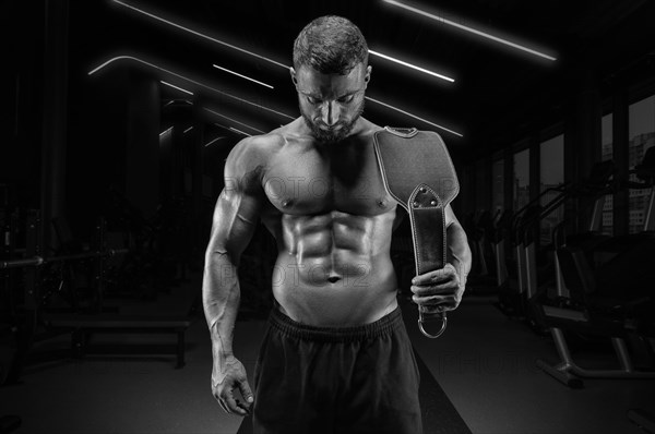 Portrait of a muscular guy with a naked torso and abs. Gym. Athletic chain belt. Fitness concept