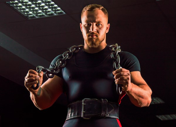 Huge weightlifter with a chain around his neck is in the gym