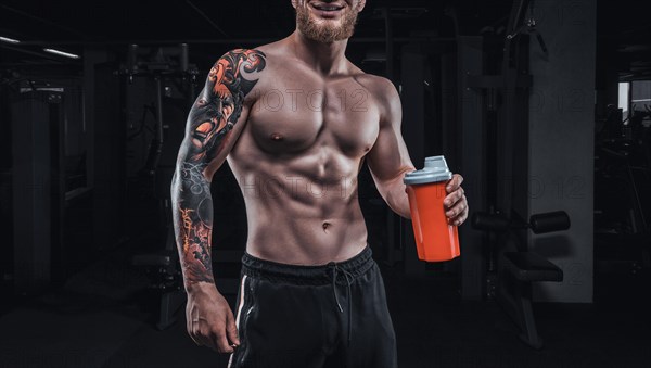 Portrait of an athlete standing with a shaker in the gym. Bodybuilding and fitness concept.