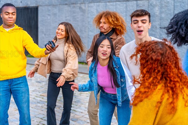 Group of young and multi-ethnic friends listening to music and dancing in the street