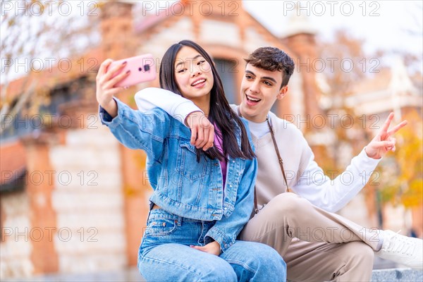 Joyful multi-ethnic couple taking a selfie with the mobile phone sitting in the street