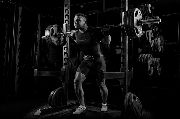 The weightlifter is preparing to lift a very heavy barbell. He exhales breathlessly and strains as much as possible before performing the exercise