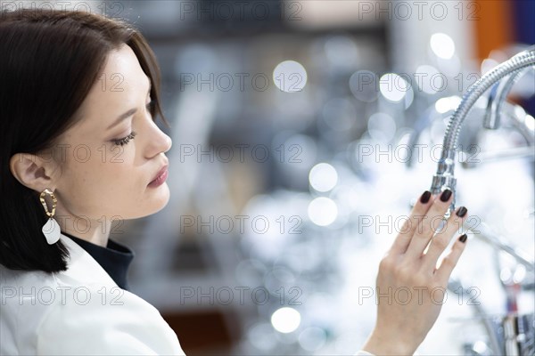 Beautiful young woman in a white jacket chooses plumbing supplies in a hardware store