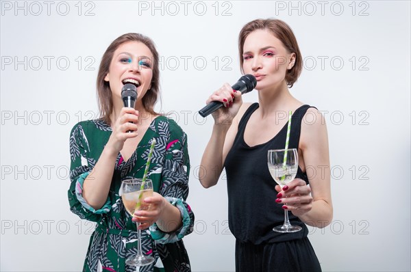 Portrait of two singing girls with glasses in their hands. Karaoke concept.