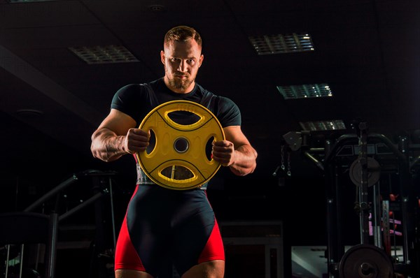 Huge weightlifter stands with a weight for the bar in the gym