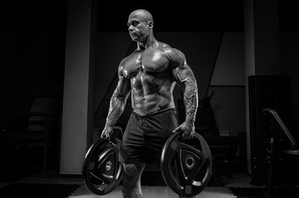 Muscular man stands in a gym with barbell discs. Bodybuilding and powerlifting concept.