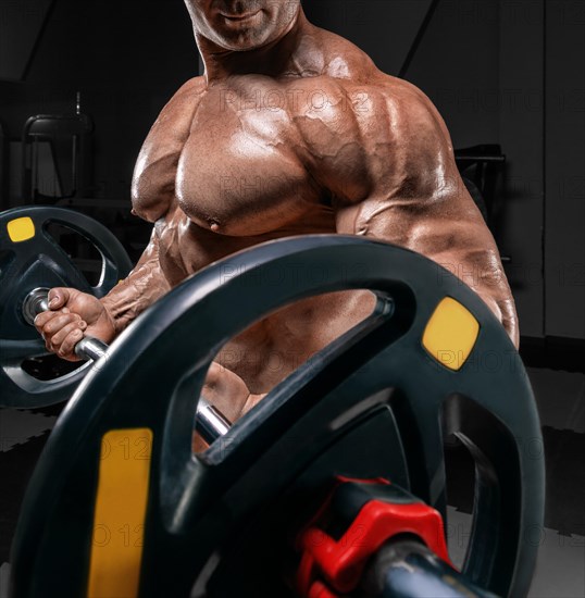 Powerful bodybuilder trains in a gym with a barbell. No name portrait. Bodybuilding concept.