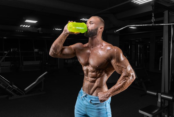 The athlete poses in the gym with a shaker in his hand. Fitness