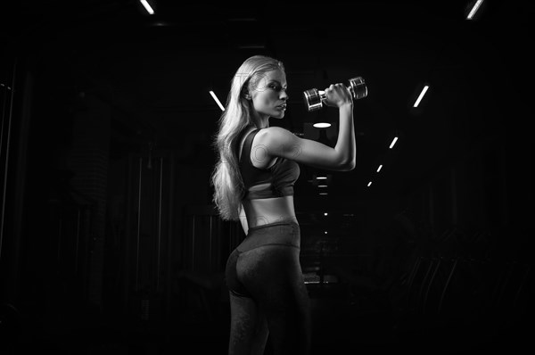Charming sportswoman posing in the gym with dumbbells. The concept of bodybuilding