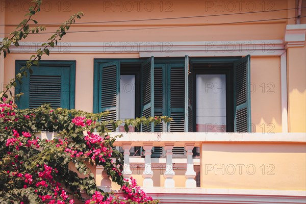 Sunny facade of a pink Mediterranean building with blue shutters and blooming bougainvillea