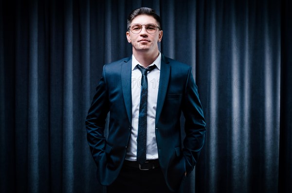 Adult man is standing in a suit against a black curtain. Business concept. The administrative staff of the company.