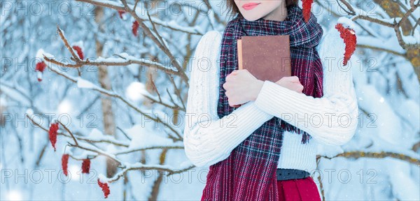 No name portrait of a charming girl who hugs a book in the winter forest. Concept of Christmas