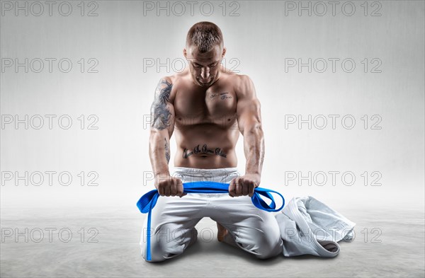 Professional athlete sits in the gym in a kimono with a blue belt. Concept of karate