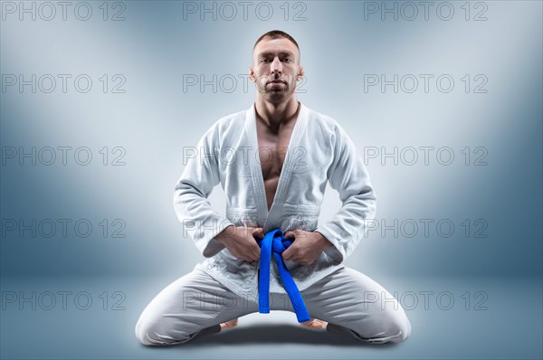 Athlete in a kimono with a blue belt sits and waits for the opponent. Concept of karate