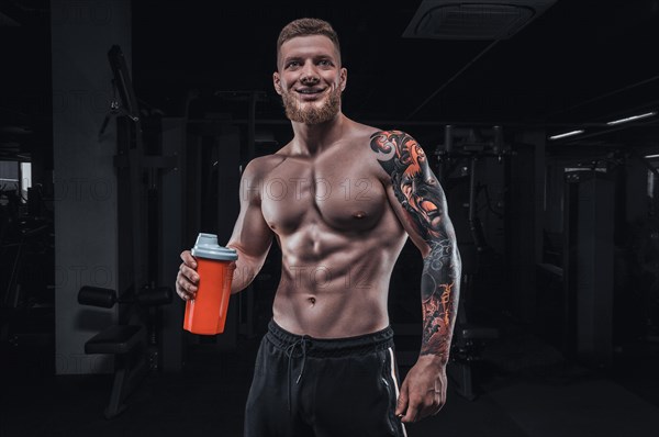 Portrait of an athlete standing with a shaker in the gym. Bodybuilding and fitness concept.
