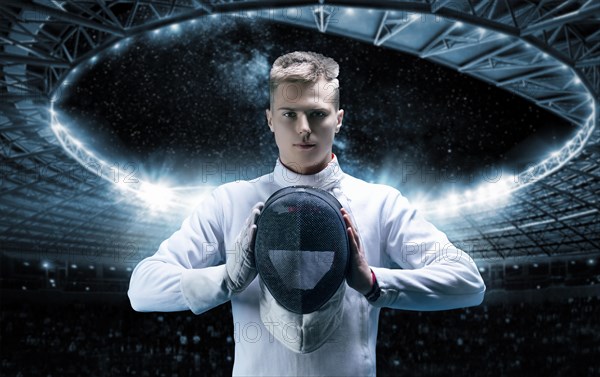 Portrait of a male fencer on the background of a sports arena. He holds a helmet in front of him. The concept of fencing.