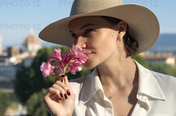 Portrait of a charming girl standing on Piazzale Michelangelo in Florence. She sniffs flowers and looks forward. The concept of tourism