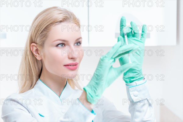 Portrait of a blonde girl in a medical gown with a syringe in her hands. Medical center advertisement.