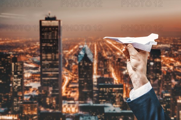 Image of a man's hand in a suit. He launches a paper airplane from the roof of a skyscraper. Business concept.