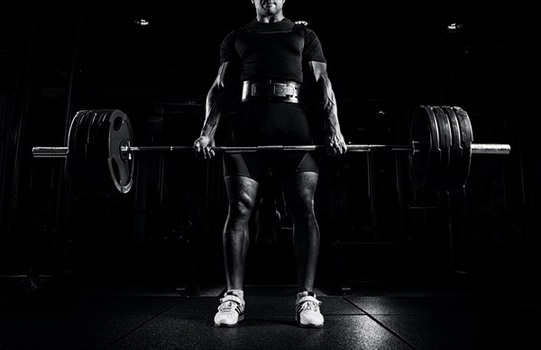 Professional athlete is standing and is holding a very heavy barbell. Front view