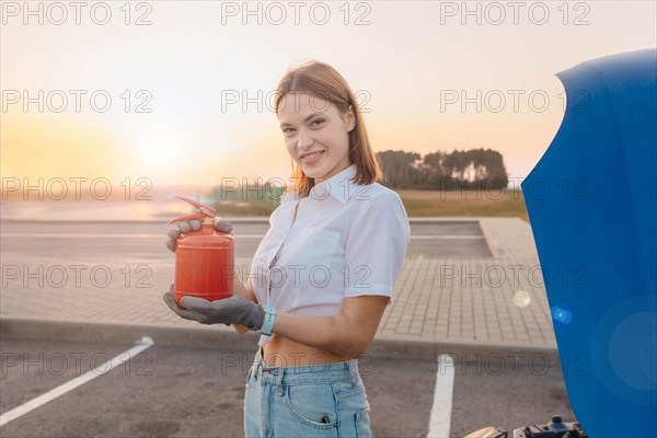 Young beautiful and hot woman driver holds a fire extinguisher in her hands