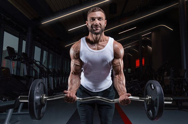 Handsome young man working out with a barbell in the gym. Biceps pumping. Fitness and bodybuilding concept.