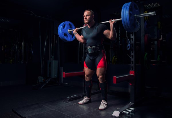 Professional athlete makes squats with a bar in the gym