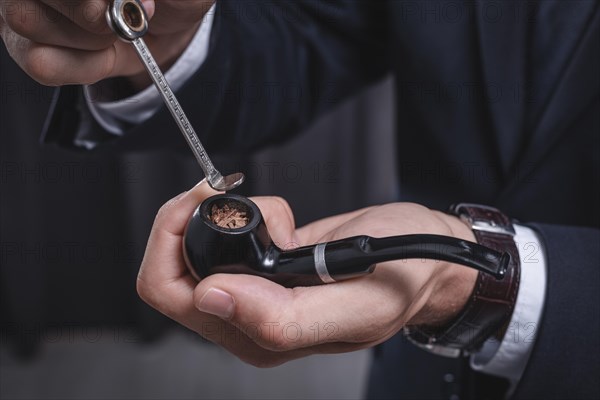 Image of male hands holding a smoking pipe and tamper. Tobacco smoking concept.