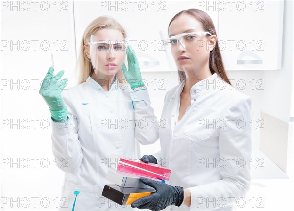 Two beauticians pose in a medical office with cosmetic preparations and a syringe. Skin rejuvenation concept.