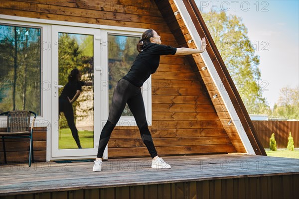 Attractive fit sporty woman doing workout on the terrace of bungalow on sunny day