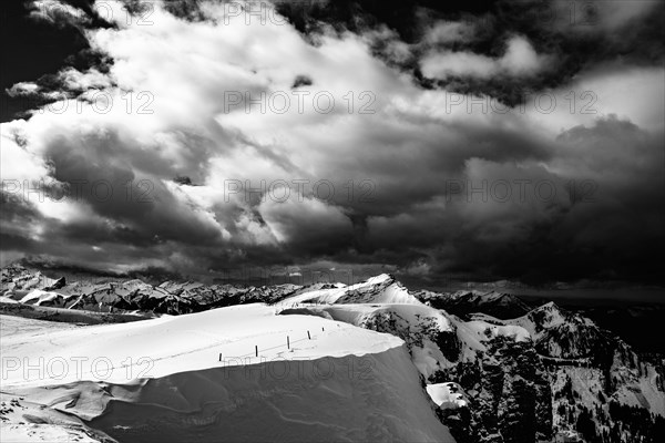 Berlinger Koepfl summit area with snow-covered mountains in the background and dramatic sky