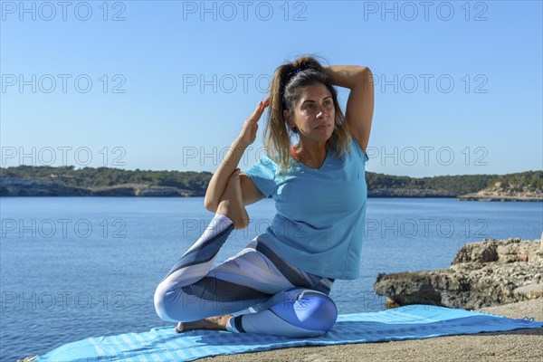 Middle-aged fitness woman outdoors in front of the sea does yoga stretching exercises