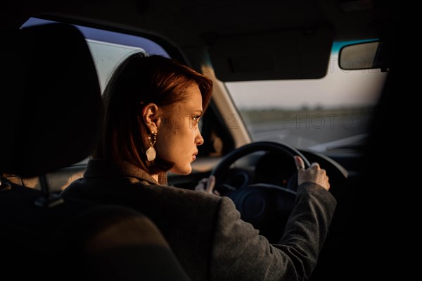 Young beautiful smiling woman taxi driver in a jacket sits behind the wheel of a car and looks at the road