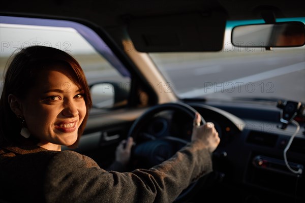 Young beautiful smiling female taxi driver in a jacket greets passengers in a friendly manner