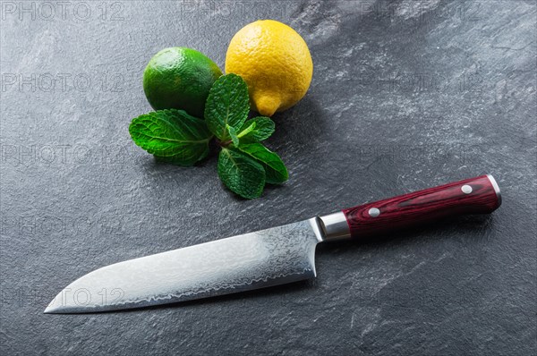 Japanese knife made of Damascus steel lies on a table near mint and citrus. View from above