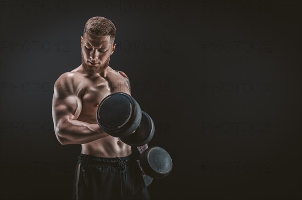 Young muscular guy pumping biceps with dumbbells. Concentrated flexion. Fitness and nutrition concept.