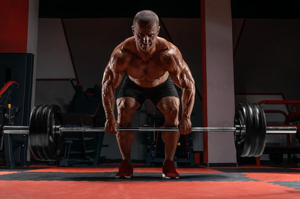 Muscular man trains in the gym with a barbell in his hands. Deadlift. Bodybuilding concept.