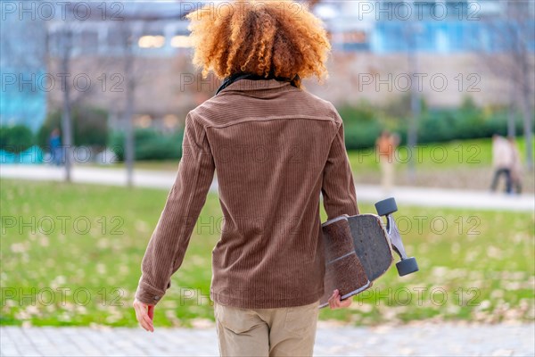 Rear view of a man carrying a skateboard in a park