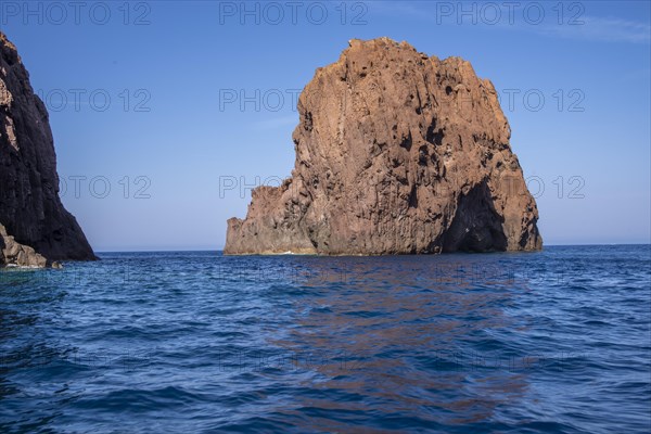 View of the red rocks in the Scandola nature reserve in the deep blue sea under a clear blue sky
