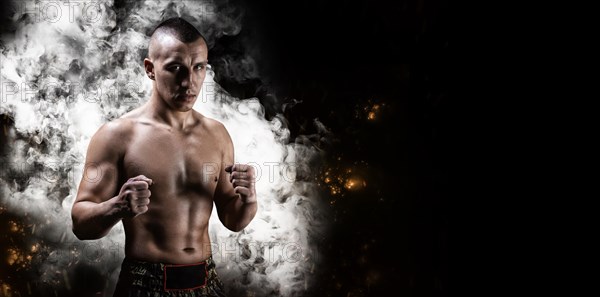 Portrait of a boxer of mixed martial arts standing on the background of smoke and fire. The concept of sports